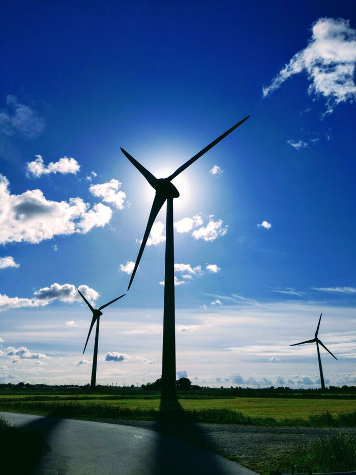our-mission Photo of wind turbines silhouetted against a blue sky with clouds, symbolizing renewable energy.