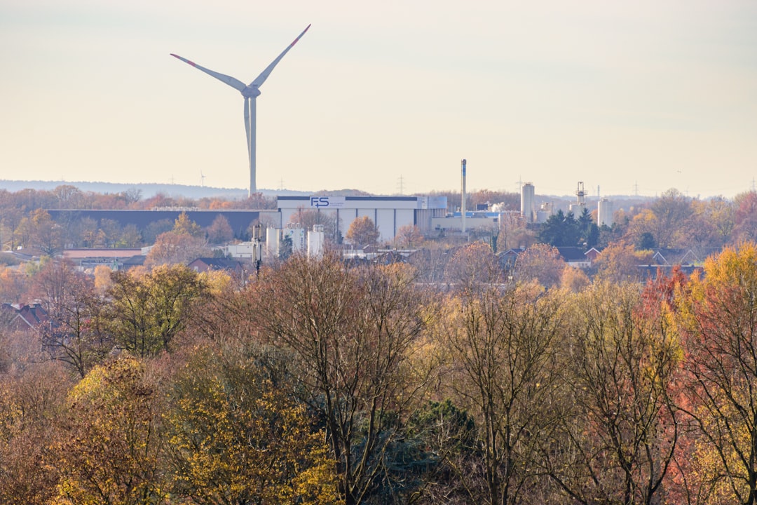wind-turbine-above-autumn-trees-and-industrial-buildings-rmxmm9sabpe